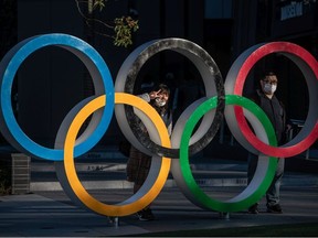 People wearing face masks pose for photographs next to Olympic Rings on March 24, 2020 in Tokyo, Japan.