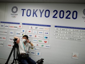 A cameraman wearing a protective face mask, following an outbreak of the coronavirus disease (COVID-19), pauses in front of placard displaying company logs of the Tokyo 2020 Olympic and Paralympic Games partners and supporters at a news conference site in Tokyo, Japan March 17, 2020.   REUTERS/Issei Kato