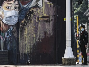 A member of the special forces police wears a face mask against the spread of the new coronavirus as he stands guard in front of a mural depicting a person wearing a face mask in Bogota on March 21, 2020.  (JUAN BARRETO/AFP via Getty Images)
