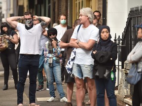 A man, left, puts on a mask as he joins a queue outside a benefits payment centre in Sydney on March 23, 2020. (PETER PARKS/AFP via Getty Images)