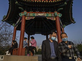 People wear protective masks as they sit and walk near an overlook at Ritan Park, in Beijing, China, on Sunday, March 22, 2020.