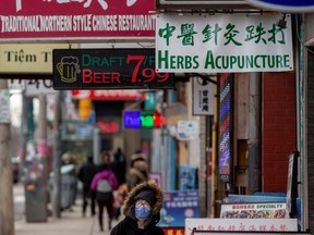 A woman, wearing a mask, walks in the Chinatown district of downtown Toronto, Ontario.