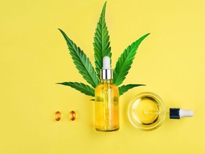 Bottle with CBD oil, pipette, capsules and cannabis leaf on a yellow background. Minimalism, flat lay.