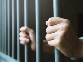 A prisoner grasps cell bars.