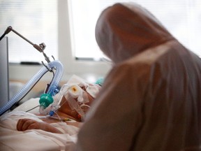 A medical worker in a protective suit treats a patient suffering with coronavirus in an intensive care unit at the Casalpalocco hospital in Rome March 24, 2020. (REUTERS/Guglielmo Mangiapane)