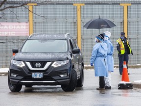 Health-care workers use an umbrella to stay dry while speaking to people in their cars at the Carling Heights Optimist Community Centre COVID 19 assessment centre  in London, Ont. on Monday March 23, 2020.  Derek Ruttan/Postmedia Network