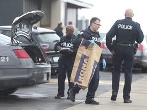 A group of Toronto Police officers huddle around a cruiser as they remove two swords from the trunk at the scene of a violent attack at a Commercial Bakeries Corp. on Friday, March 20, 2020. (Jack Boland/Toronto SUn)