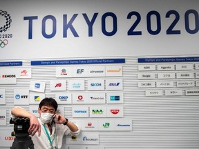 A reporter wearing a face mask speaks on his phone as he sits next to the company logos of the Tokyo Olympic and Paralympic Games gold and official partners during a Tokyo 2020 press conference about the spread of the new coronavirus in Tokyo on Tuesday, March 17, 2020.