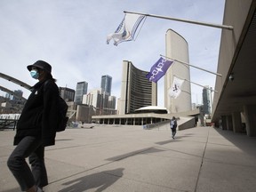 A small group of pedestrians pass through Nathan Phillips Square in front of Toronto City Hall on Monday, March 16, 2020.