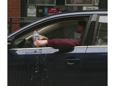 A motorist parked at the northwest corner of College St. E. and Yonge St. wearing a mask and gloves cleans off their hands with a large bottle of water on Thursday March 26, 2020. Jack Boland/Toronto Sun/Postmedia Network