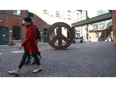 A couple and their dog enjoy the sunny weather at the Gooderham and Worts Distillery District as they walk past the Peace Sculpture. There was a brisk wind and the temperature got up to 10C by mid afternoon on Friday March 27, 2020. Jack Boland/Toronto Sun/Postmedia Network