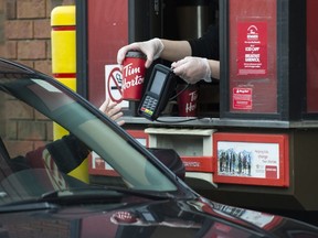 A Tim Hortons employee hands out coffee at a   drive-thru in Mississauga on March 17, 2020. (The Canadian Press)