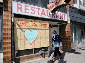 A man wearing a protective face mask passes a boarded up restaurant in Toronto on April 6, 2020. (Reuters)