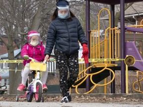 A woman and child wearing masks and full face shields pass a taped off play structure in Toronto on Thursday March 26, 2020. THE CANADIAN PRESS/Frank Gunn