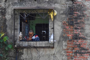 A man checks his mobile phone standing by a window of his tenement at the Dharavi slum during a government-imposed nationwide lockdown as a preventive measure against the spread of the COVID-19 coronavirus in Mumbai on April 8, 2020. - Amidst the clogged drains and overflowing garbage dumps of Mumbai's Dharavi -- one of Asia's largest slums -- coronavirus fears are growing, and residents say they are powerless to stop the spread of the disease. The warren of narrow alleys in India's financial capital -- made famous by the 2008 Oscar-winning film "Slumdog Millionaire" -- is home to around a million people, many of whom work as security guards or domestic workers in upmarket neighbourhoods nearby. The Indian government announced a lockdown across the country last month, ordering citizens to stay home in the hope that this would contain the spread of the virus. But Dharavi's crowded streets mean social distancing is near impossible for the people who live there -- even if they only leave home to buy food. (Photo by Indranil MUKHERJEE / AFP) (Photo by INDRANIL MUKHERJEE/AFP via Getty Images)