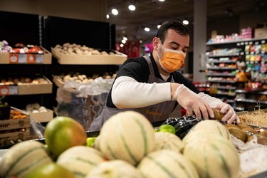 An employee wearing gloves and a protective mask across his nose and mouth arranges fruit and vegetables on a stall, in a Franprix supermarket, in Paris, on April 8, 2020, on the twenty third day of a strict lockdown in France aimed at curbing the spread of the COVID-19 pandemic, caused by the novel coronavirus. (Photo by Thomas SAMSON / AFP) (Photo by THOMAS SAMSON/AFP via Getty Images)