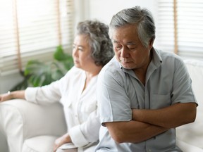 Upset Senior man sitting on sofa against the background of his wife.