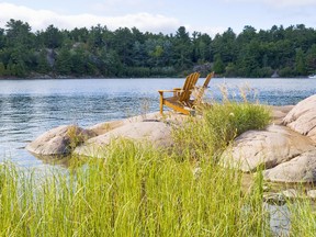 Two Muskoka/Adirondack chairs sitting on big smooth pink granites by the lake.