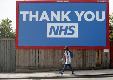 A person wearing a protective face mask walks past a billboard with a message reading "Thank you NHS" in Kilburn, as the spread of the coronavirus disease (COVID-19) continues, London, Britain, April 8, 2020. REUTERS/Paul Childs ORG XMIT: AI