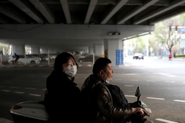 A woman wearing a face mask sits behind a man on a vehicle near Beijing's Financial Street in Beijing, as the spread of the novel coronavirus disease (COVID-19) continues in the country, China April 8, 2020. REUTERS/Tingshu Wang ORG XMIT: PPP-TSPEK08