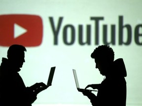 Silhouettes of mobile device users are seen next to a screen projection of Youtube logo in this picture illustration taken March 28, 2018.
