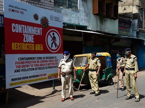 Gujarat police personnel wearing facemasks stand guard near a board reading 'Containment Zone restricted area' during a government-imposed nationwide lockdown as a preventive measure against the COVID-19 coronavirus, in Ahmedabad on April 10, 2020.