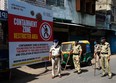 Gujarat police personnel wearing facemasks stand guard near a board reading 'Containment Zone restricted area' during a government-imposed nationwide lockdown as a preventive measure against the COVID-19 coronavirus, in Ahmedabad on April 10, 2020.