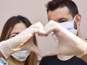 Couple wearing masks and gloves form a heart sign.