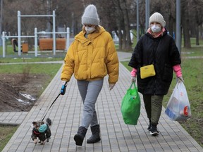 Women wearing protective masks, used as a preventive measure against coronavirus, walk with a dog in a mask, after shopping in Moscow April 2, 2020. (REUTERS/Tatyana Makeyeva)
