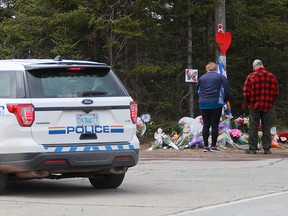 Mourners pay their respects in front of the makeshift memorial, made in the memory for the victims of Sunday’s mass shooting as a RCMP vehicle passes nearby in Portapique, N.S., on April 23, 2020.