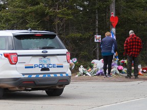 Trauernde erweisen ihren Respekt vor dem provisorischen Denkmal, das in Erinnerung an die Opfer der Massenerschießung am Sonntag errichtet wurde, als ein RCMP-Fahrzeug am 23. April 2020 in Portapique, NS, in der Nähe vorbeifährt.