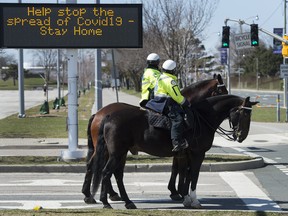 Toronto police officers stop at a red light as they patrol on their service horses in Toronto on Thursday, April 2, 2020. (THE CANADIAN PRESS/Nathan Denette)