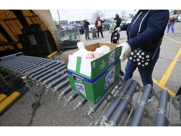 A recipient picks up a box of foodstuffs at the Toronto Daily Bread Food Bank on New Toronto St.. in Etobicoke. The TDBFB has set up an inflatable medical tent outside its facility along with a conveyor belt to get food to its clients since they cannot come in the building  on Wednesday April 8, 2020. Jack Boland/Toronto Sun/Postmedia Network