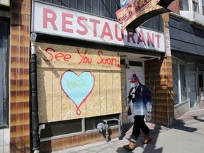 A man wearing a protective face mask passes a boarded up restaurant during the global outbreak of COVID-19 in Toronto, April 6, 2020.