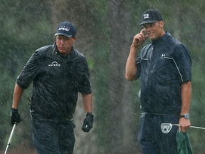 Golfer Phil Mickelson, left, and NFL player Tom Brady of the Tampa Bay Buccaneers react on the 13th green in the rain during The Match: Champions for Charity golf round at the Medalist Golf Club.