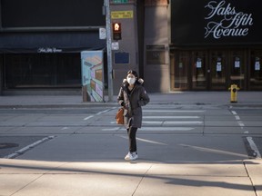 A woman wears a mask as she walks between a department store and a shopping mall in Toronto, on Saturday, March 21, 2020.