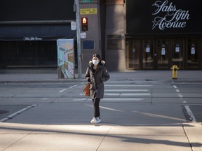 A woman wears a mask as she walks between a department store and a shopping mall in Toronto, on Saturday, March 21, 2020.