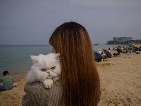 In a photo taken on May 2, 2020, a woman carries her pet cat on a beach in Sokcho, South Korea.