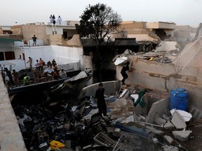 People stand on a roof of a house amidst debris of a passenger plane that crashed in a residential area near an airport in Karachi, Pakistan, on Friday, May 22, 2020.