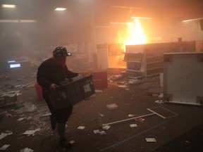 A man carries goods out of a ransacked business during protests sparked by the death of George Floyd while in police custody on Friday, May 29, 2020 in Minneapolis, Minn.