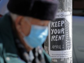 An elderly man wearing a protective face mask passes a sign publicizing a rent strike in Toronto.