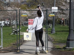 A woman takes photos of a fenced-off  Trinity Bellwoods Park in Toronto on  Thursday May 7, 2020.