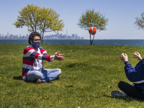 Jonathan Goldberg (left) and Samantha Rojek pass a ball back and forth while wearing masks and practicing social distancing at Cliff Lumsdon Park in Etobicoke on Wednesday, May 20, 2020.