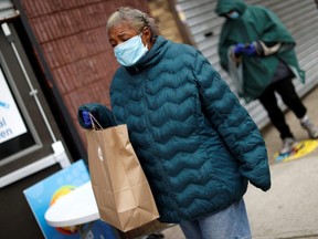 A woman carries a bag containing meals, face masks and other personal protective supplies during a distribution to residents in need outside the NAN Newark Tech World during the outbreak of COVID-19 in Newark, N.J., Wednesday, May 6, 2020.