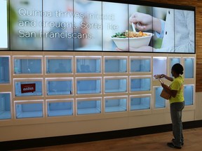 A customer picks up her lunch from an automated cubby at eatsa, a fully automated fast food restaurant on August 31, 2015 in San Francisco, California. Eatsa, an automated fast food restaurant that has no servers, wait staff and a virtual cashier that offers fresh quinoa bowls opened in San Francisco’s Financial District in 2015. Customers place their orders at an interactive kiosk and then pick their orders at a first of its kind automated food pick-up system that features a collection of glass door “cubbies” with a door that displays personalized graphics and presents the food at the touch of a button. (Photo by Justin Sullivan/Getty Images)