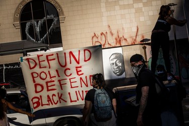 Demonstrators hang a sign next to a mural (back R) of George Floyd, who died in Minneapolis on May 25 whilst in police custody, during a "Sit Out the Curfew" protest in downtown Oakland, California on June 3, 2020. - US protesters welcomed new charges against Minneapolis officers in the killing of African-American man George Floyd -- but thousands still marched in cities across the country for a ninth straight night, chanting against racism and police brutality.