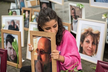 Syrian campaigner Wafa Mustafa sits between pictures of victims of the Syrian regime as she holds a picture of her father, during a protest outside the trial against two Syrian alleged former intelligence officers accused for crimes against humanity, in the first trial of its kind to emerge from the Syrian conflict, on June 4, 2020 in Koblenz, western Germany. - Wafa was part of the resistance against the Syrian government and had to flee Syria once her dad was arrested. She came to Germany in 2016.