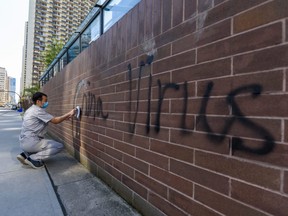 A man cleans graffiti on the Chinese consulate's wall in Calgary Wednesday, May 27, 2020.