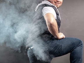 Man lift the leg and fart in front of grey background.