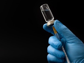 Insulin shot, flu jab or medical injection concept theme with doctor or nurse hands wearing blue surgical latex gloves filling a syringe from a glass vial isolated on black background with copyspace